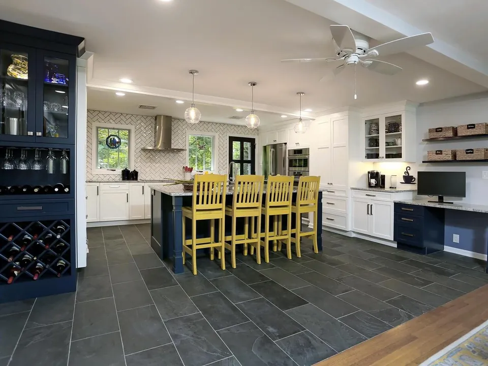 Wide view of a remodeled white kitchen with a blue island and bar seating