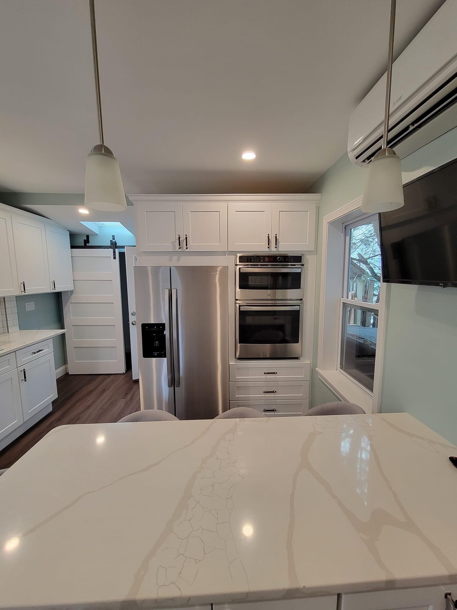 Kitchen island seating with pendant lights, built-in fridge and wall ovens beyond, North Reading