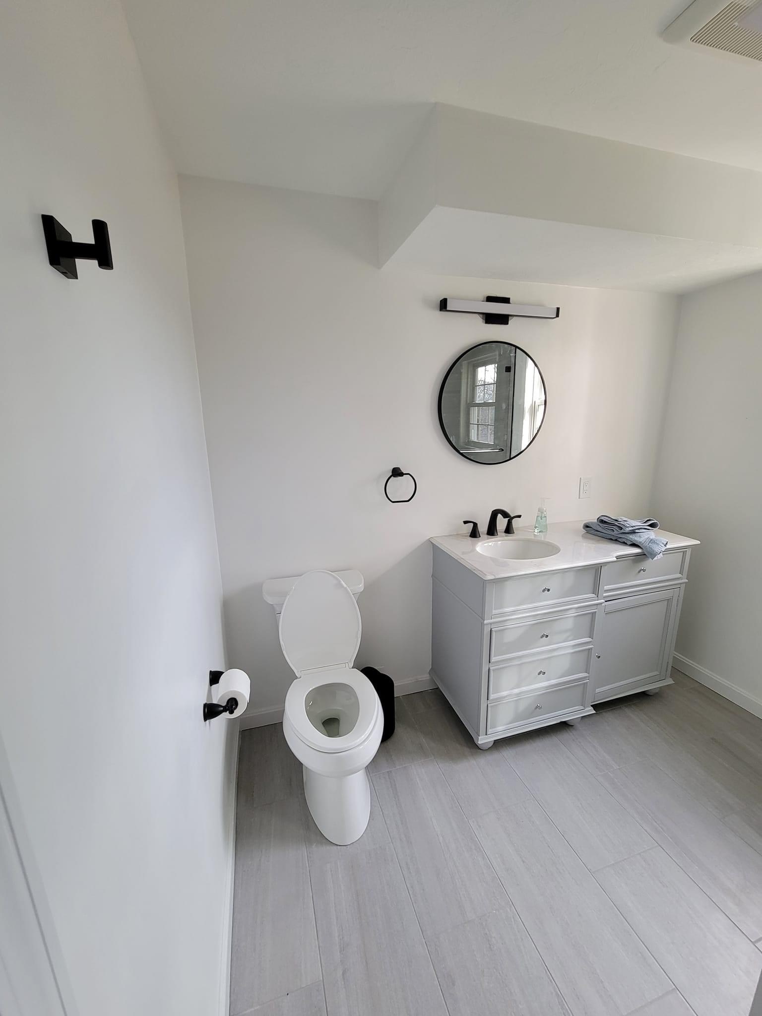 A bathroom with a gray vanity, round black-framed mirror and black fixtures, Lexington