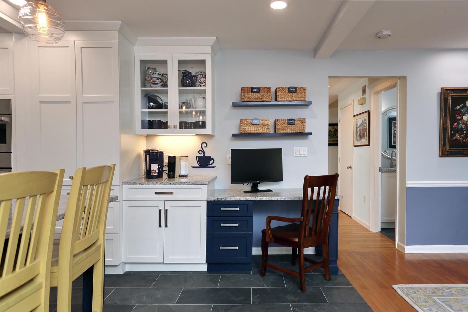Wider view of the coffee nook with glass-front cabinets, open shelving and a home-office desk area