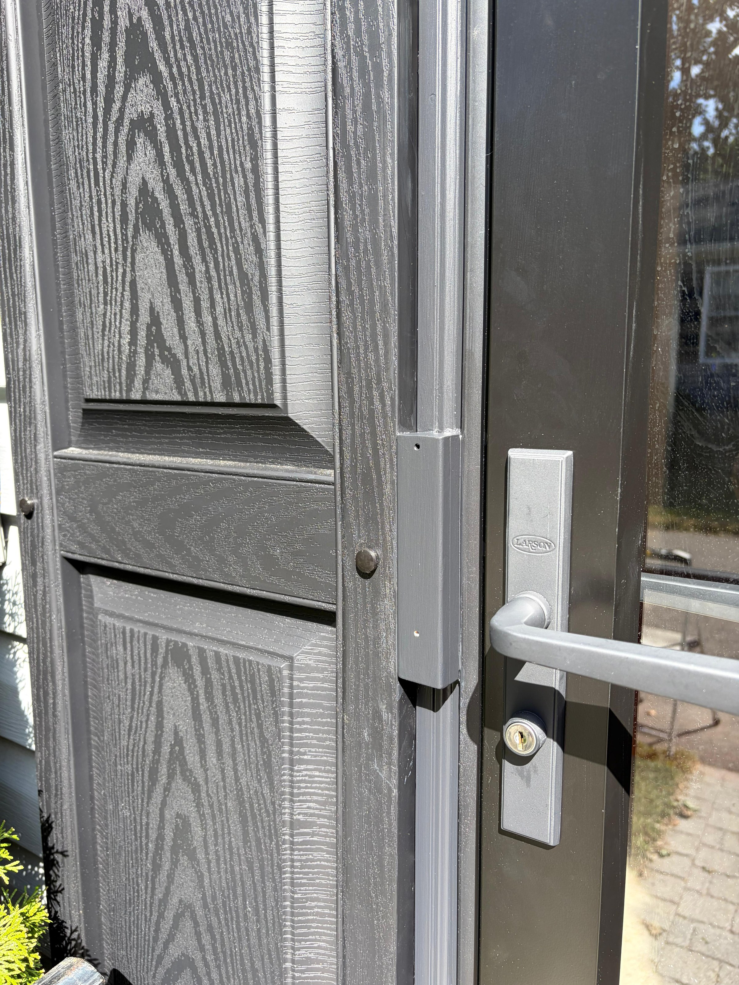 Close detail of the storm door handle, deadbolt and hinge hardware on the finished black entry, Peabody