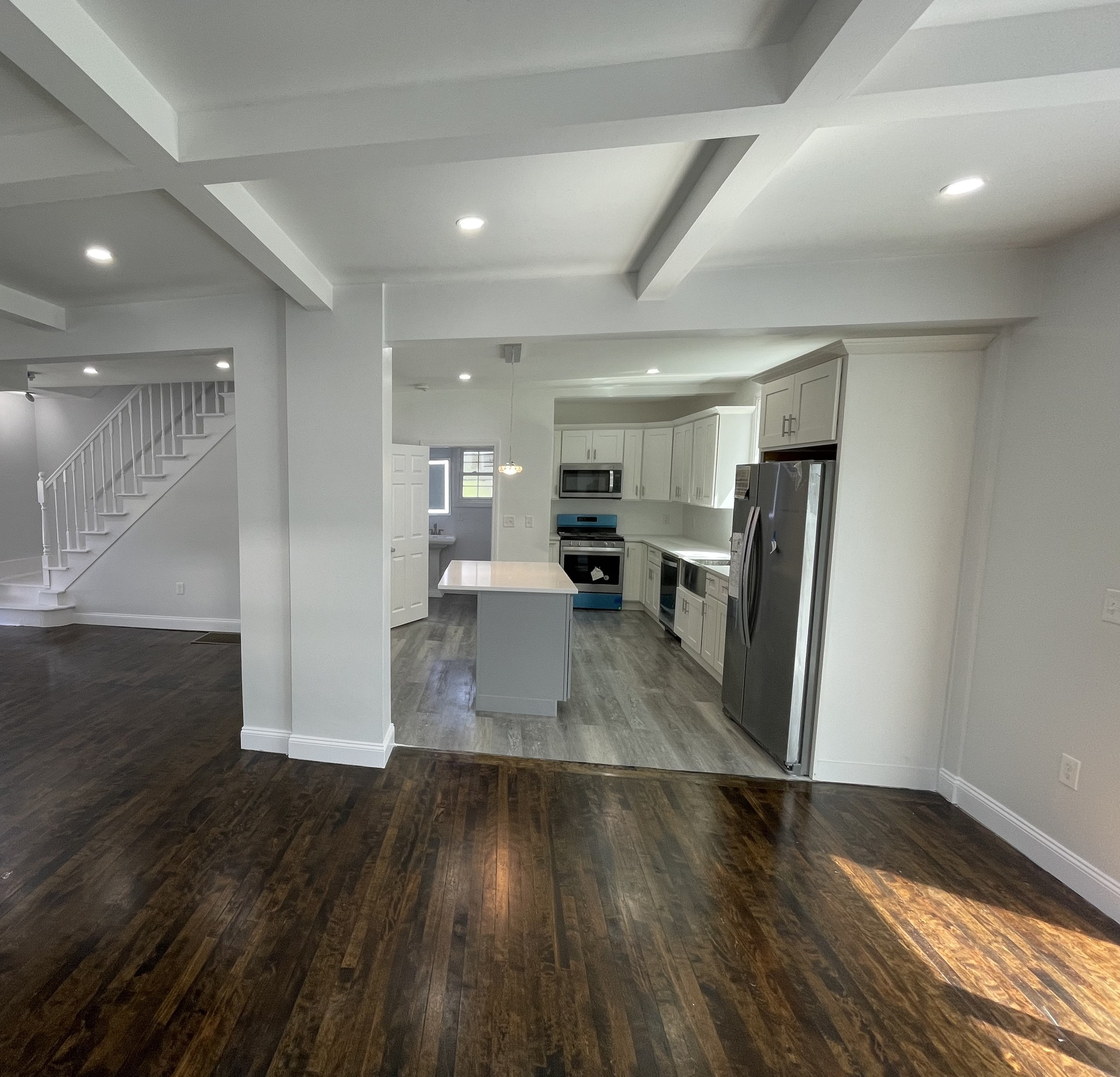 Coffered ceiling and a straight staircase opening into a small kitchen with white cabinets and a farmhouse sink