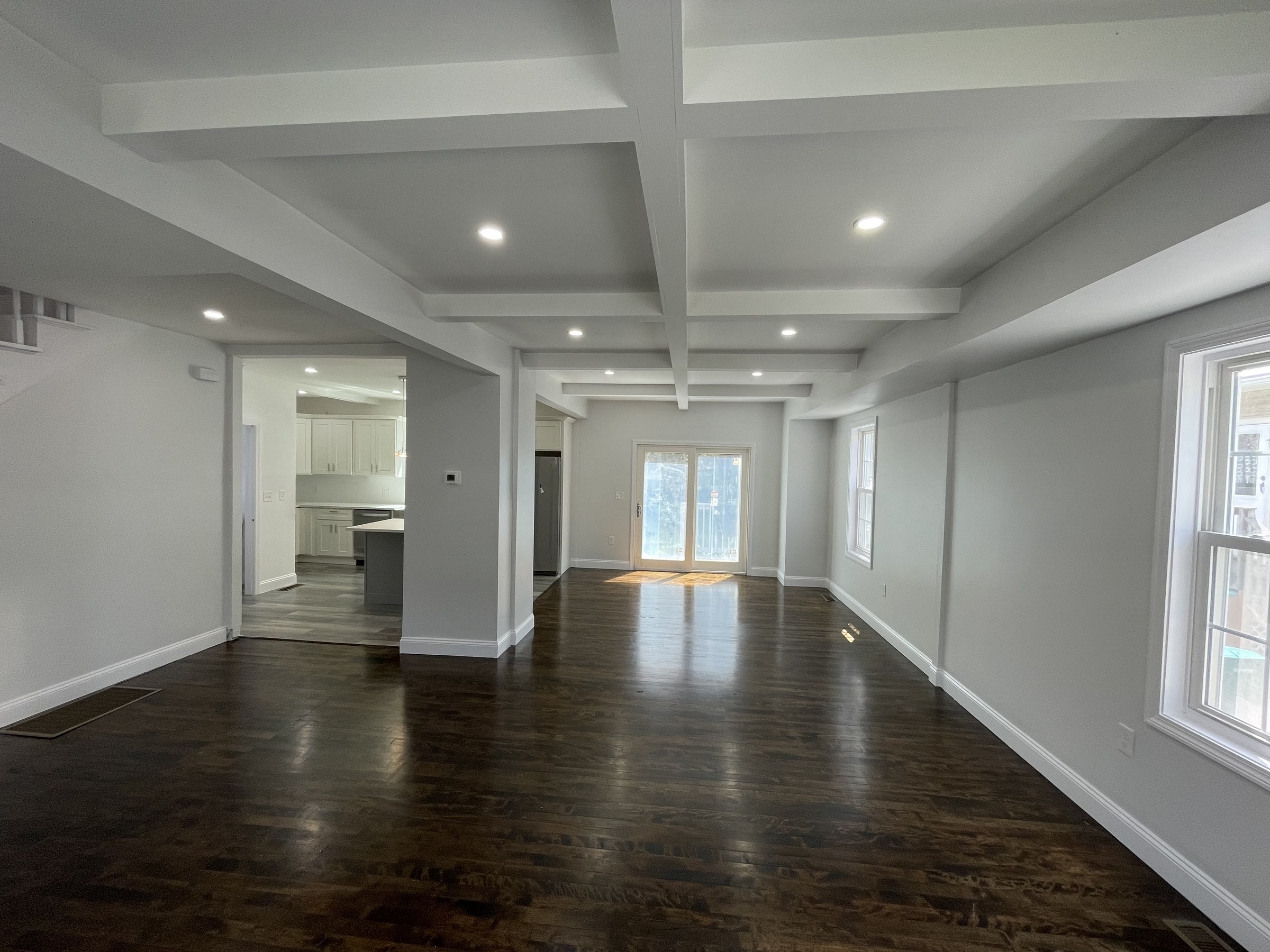 Great room with a coffered ceiling, dark hardwood floors and a sliding glass door to the backyard, a kitchen visible through an opening