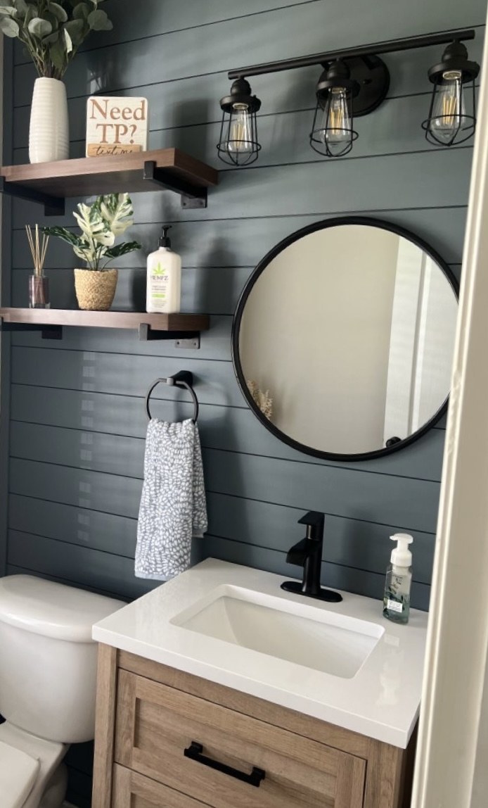 Navy shiplap-paneled powder room with a round black-framed mirror and matte black fixtures