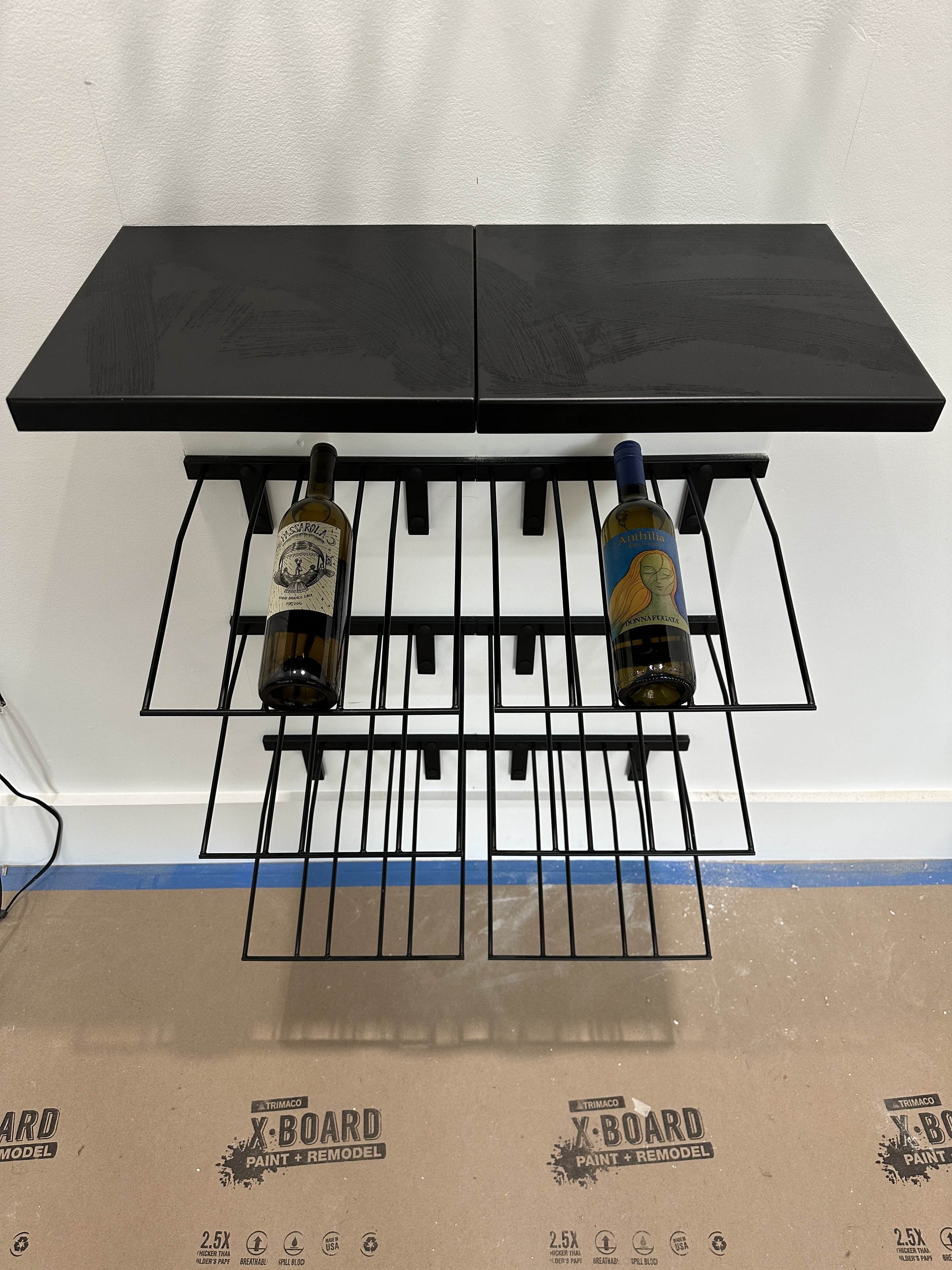 Wall-mounted wire wine bottle rack with two bottles in place, part of the room's storage