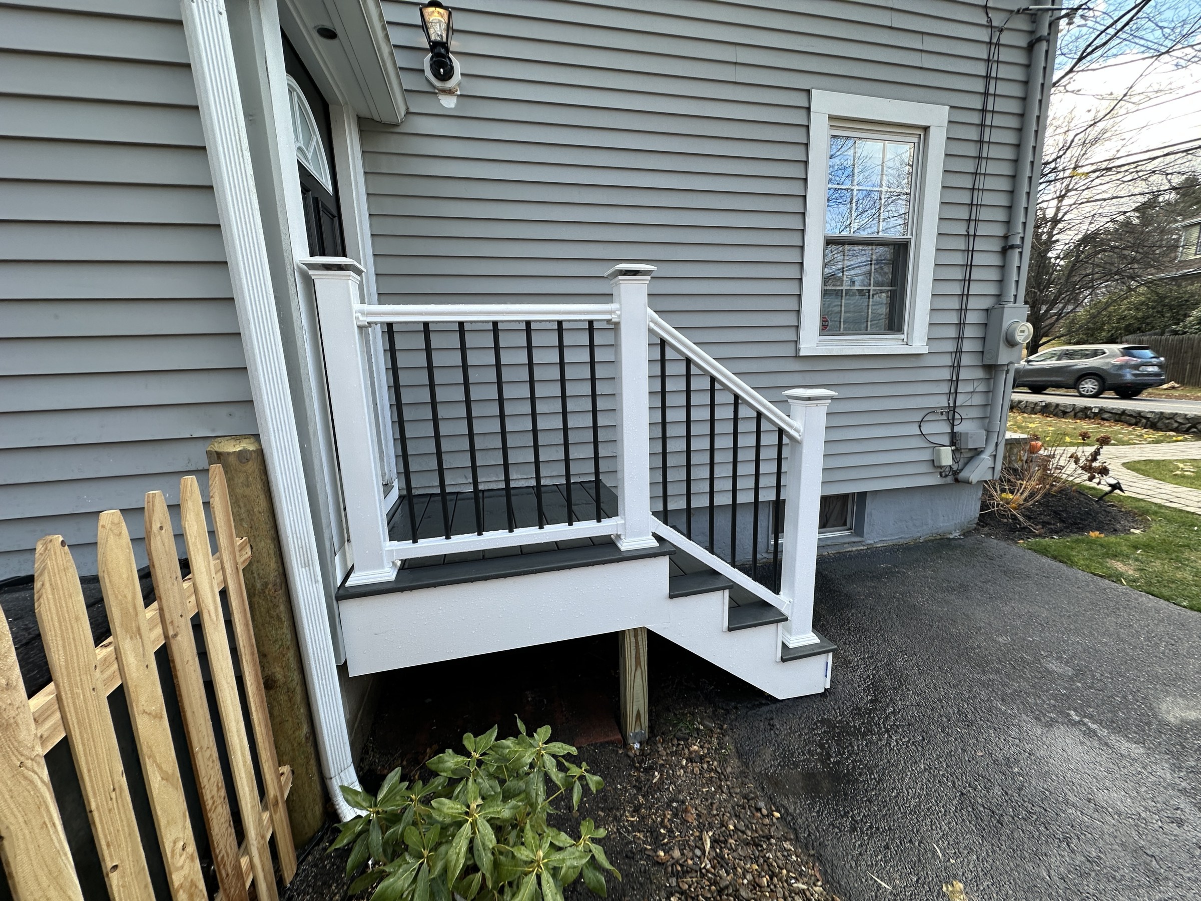 Finished entry steps viewed from the driveway, showing the full stair run down to grade with the white railing and black balusters, Reading