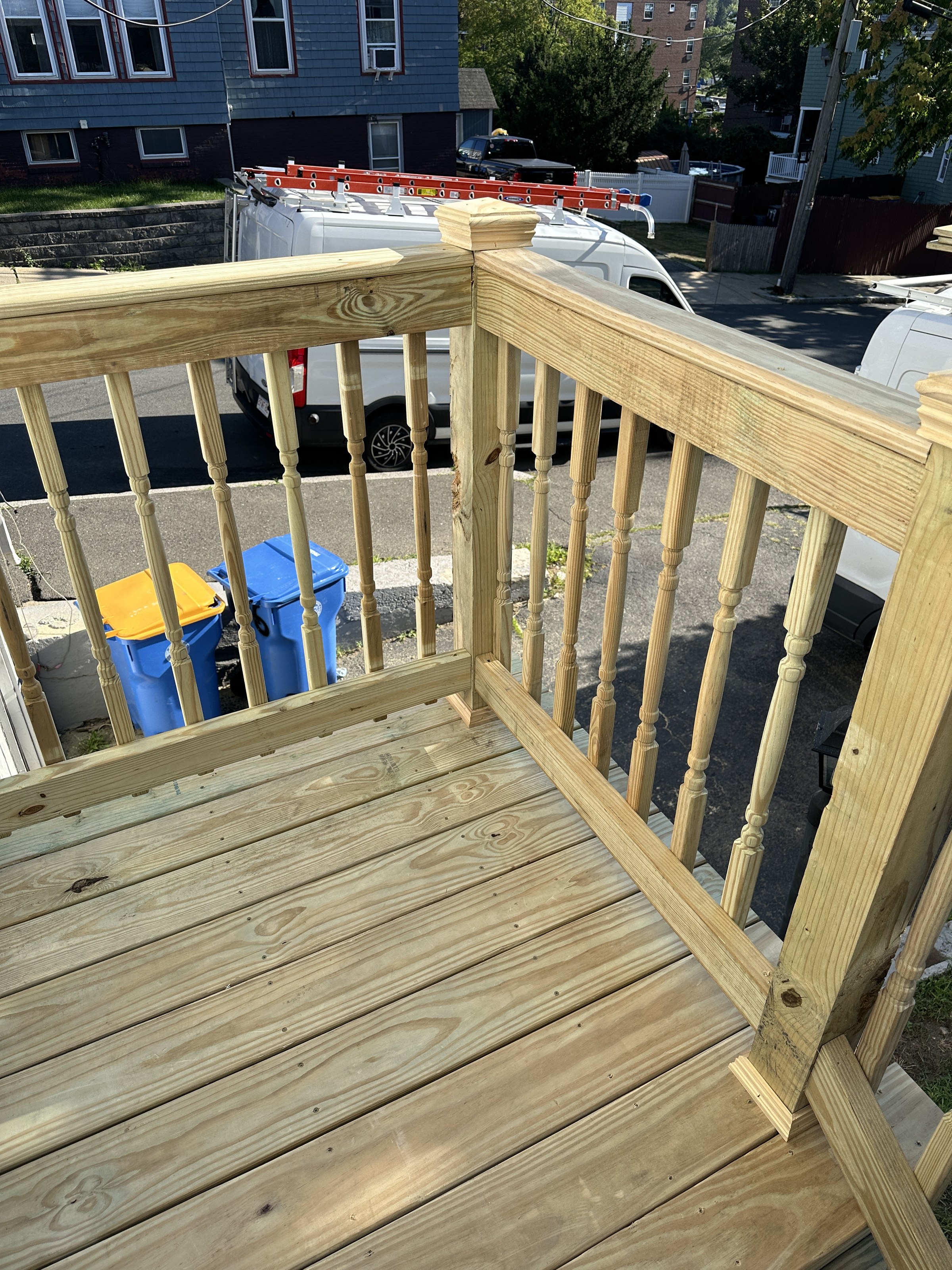 Detail of turned pressure-treated wood balusters and a capped newel post on the new deck railing, seen from above the stairs