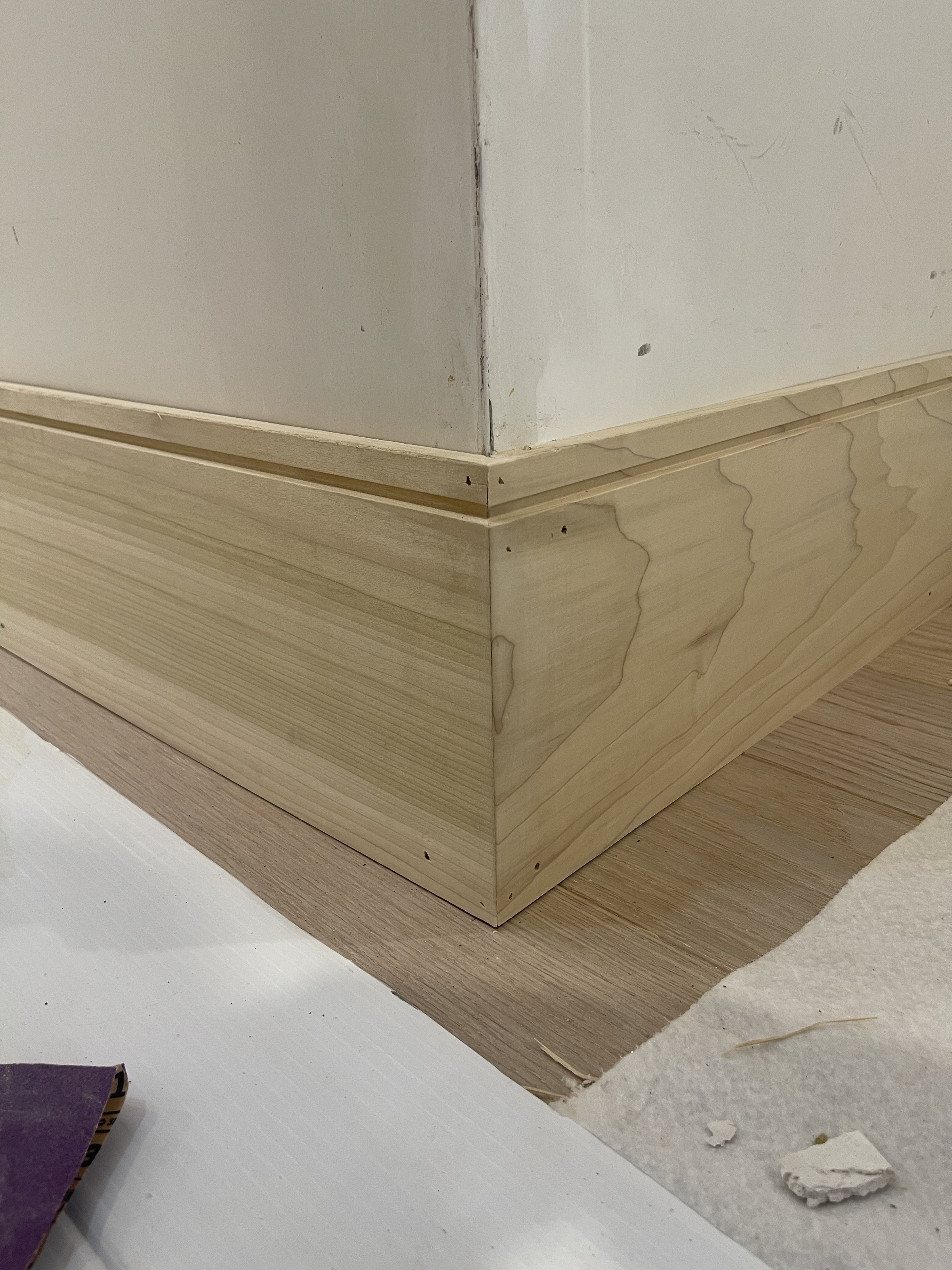 Mitered corner joint of raw, unpainted wainscoting and baseboard, floor protection paper still down, Reading