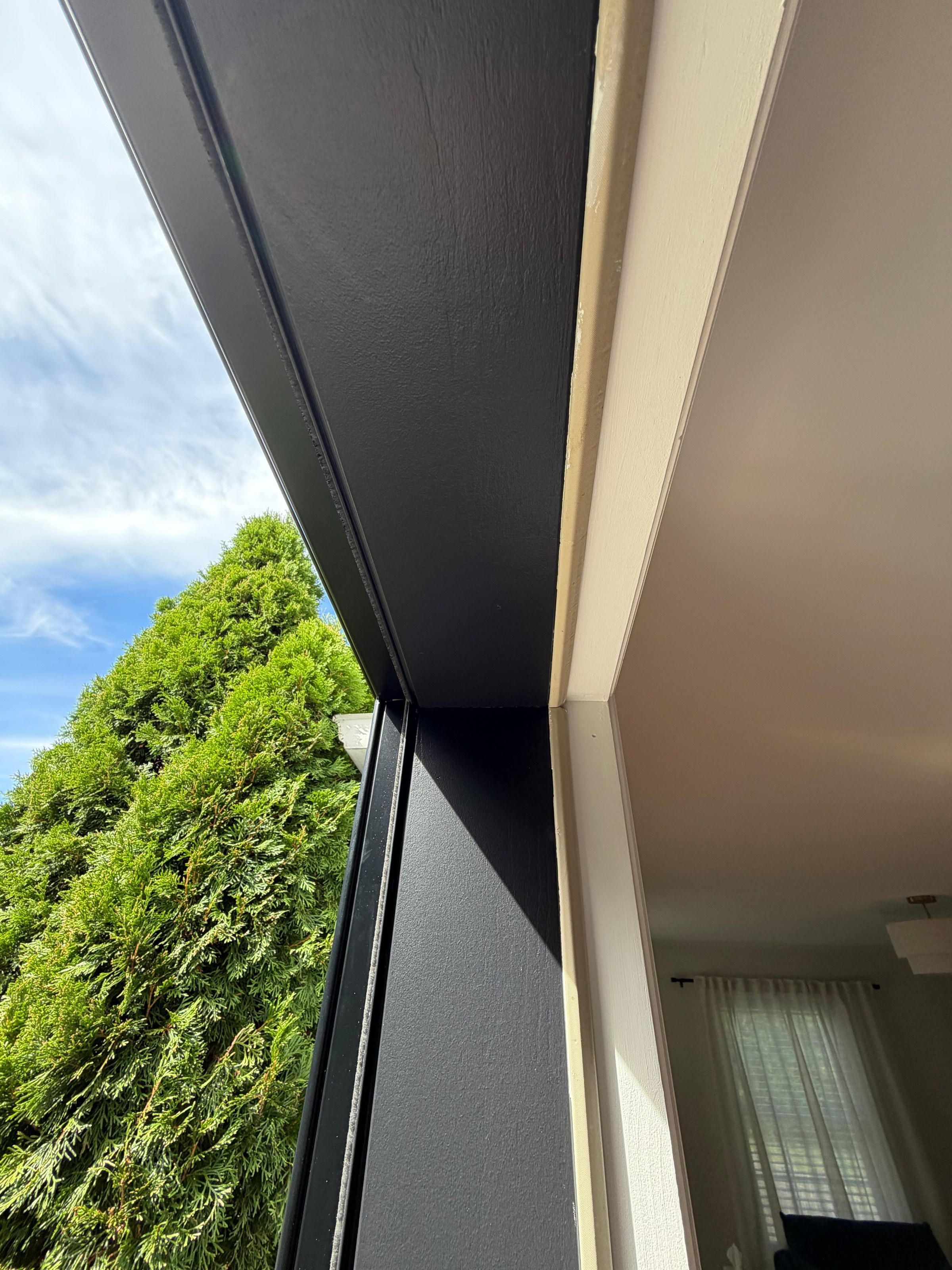 View from inside looking up at the new black head casing and jamb against the sky and hedge, Peabody