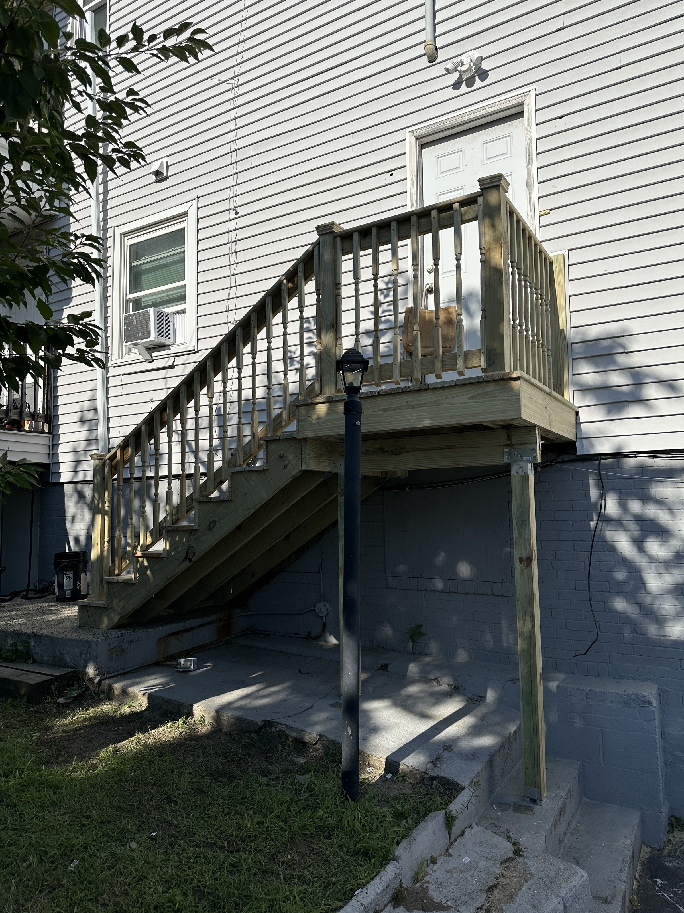 Wide establishing view of the finished exterior staircase from ground level, turned balusters and capped newel posts, a lamppost in the foreground