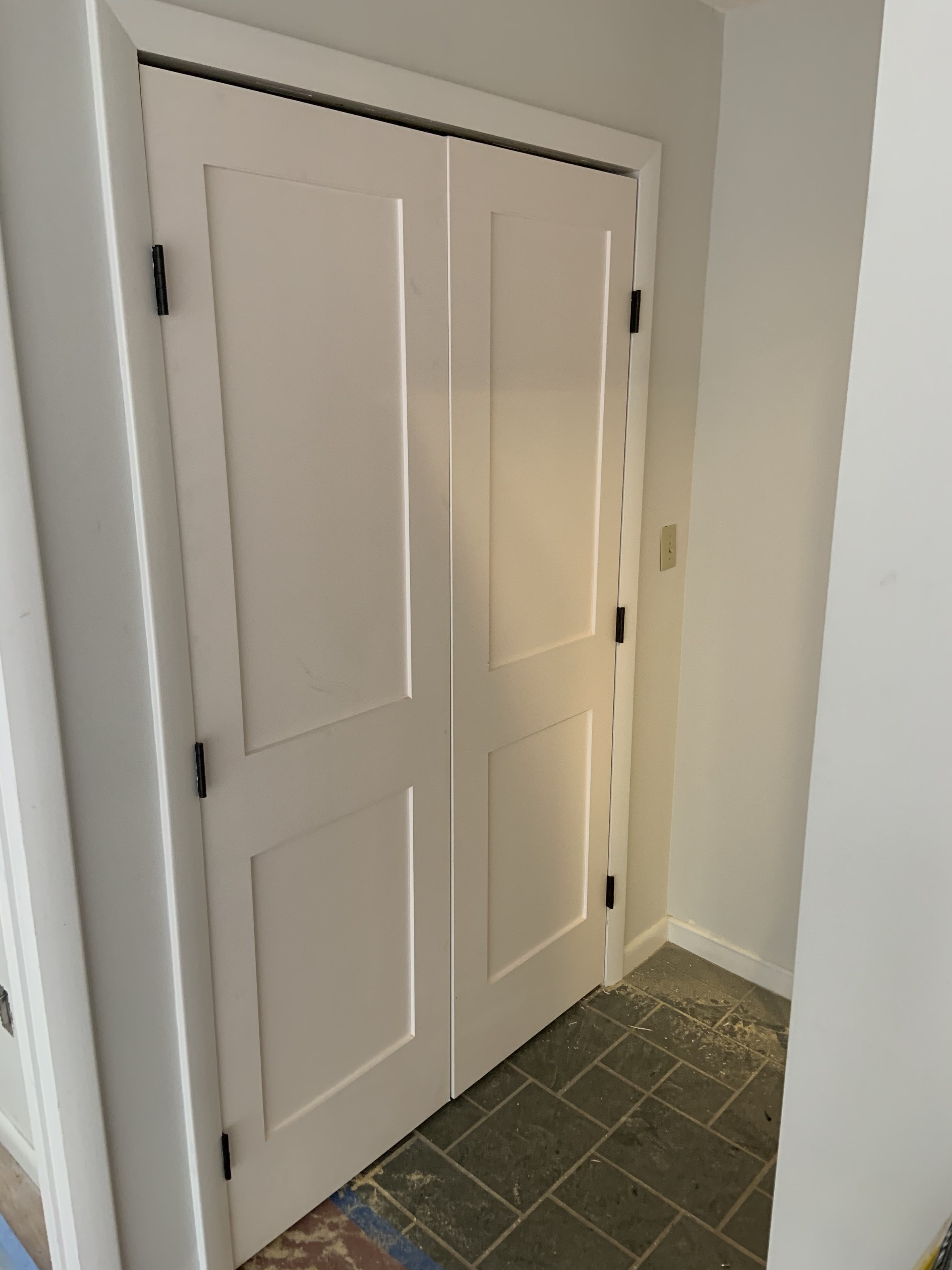 Painted bifold doors installed during the renovation, two-panel shaker style with black hardware; floor still under construction dust