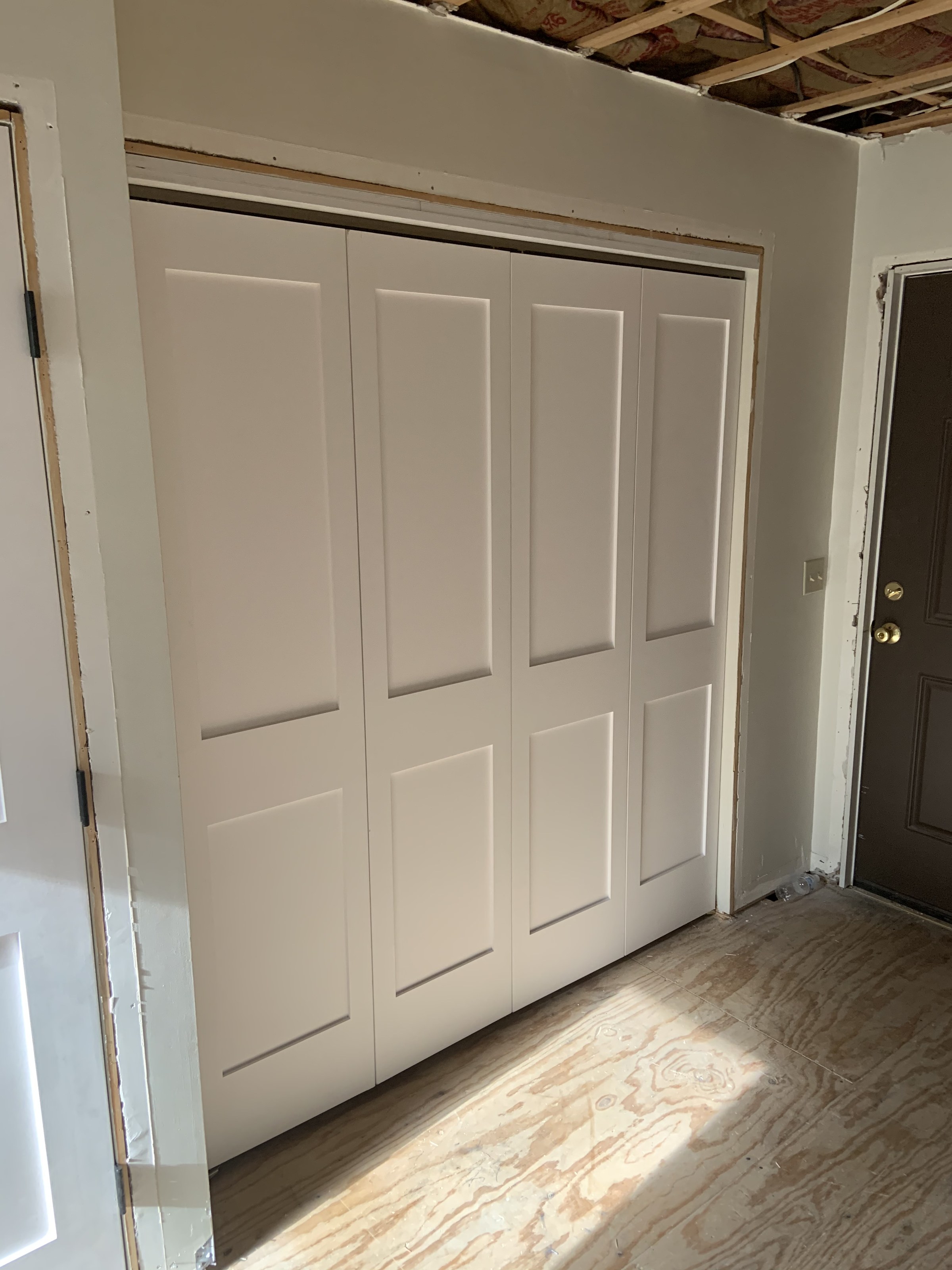 Second closet's four-panel bifold doors installed and painted while the room around them was still mid-renovation: subfloor down, ceiling not yet closed up