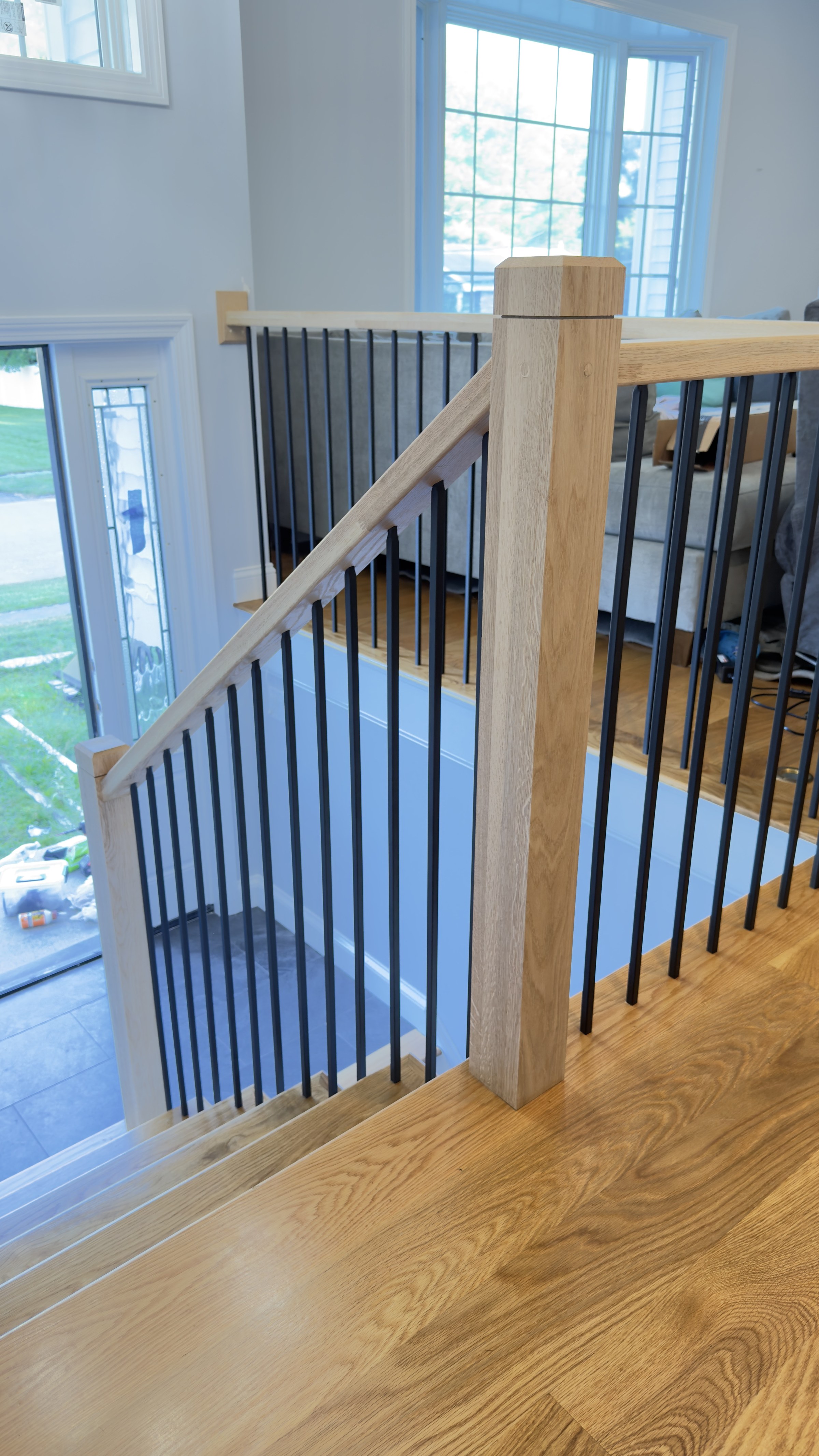 White oak top rail and newel post at the stair landing, overlooking the living room and stone fireplace below