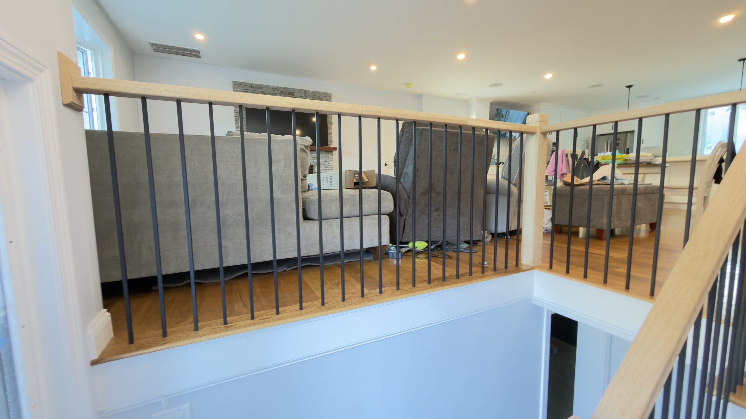 White oak rail and balusters at the stair landing, opening the sightline through to the open-plan kitchen and dining area beyond