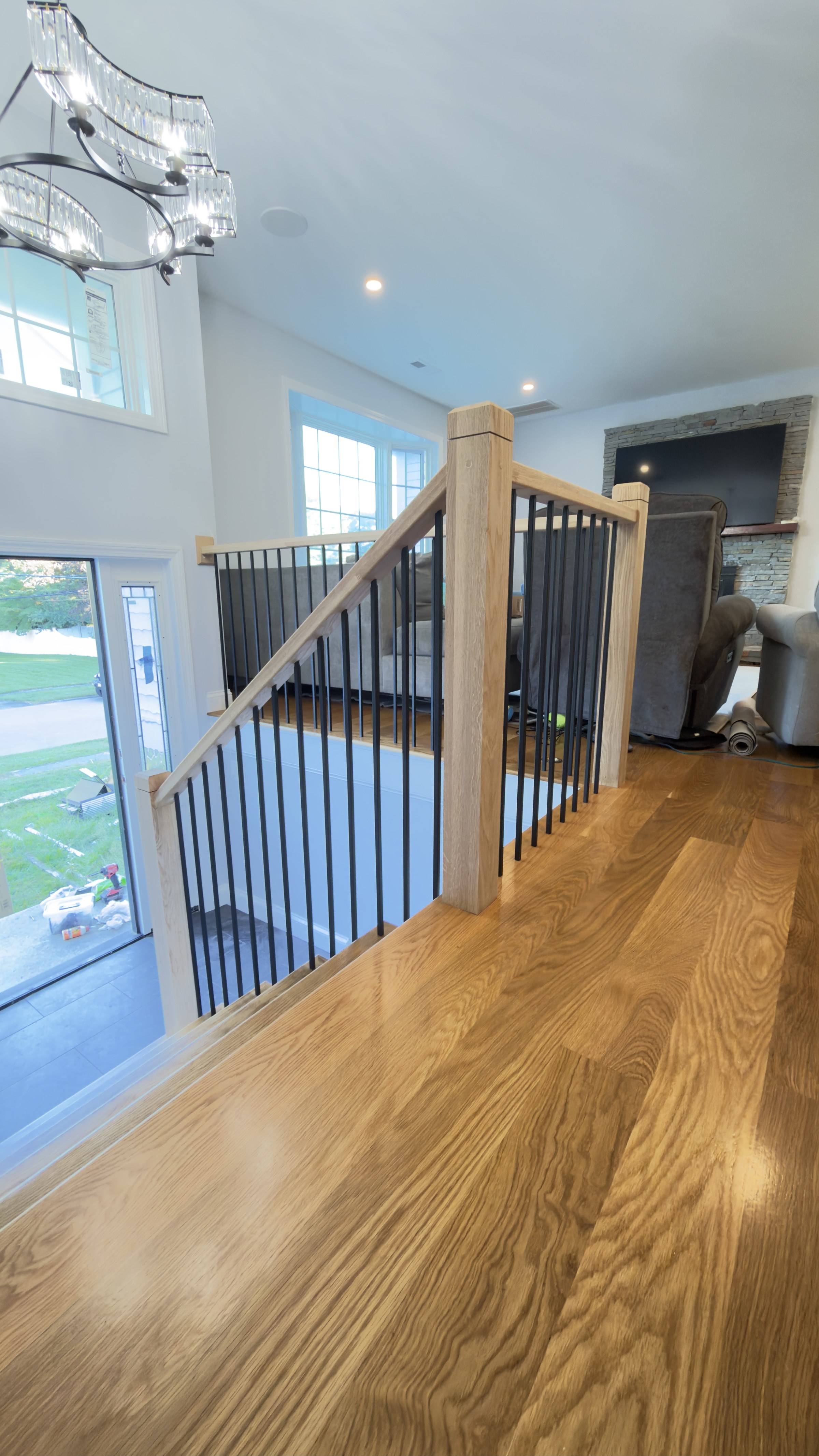 Full run of the white oak stair rail from the upper landing down to the bottom, a chandelier and bay window in the background