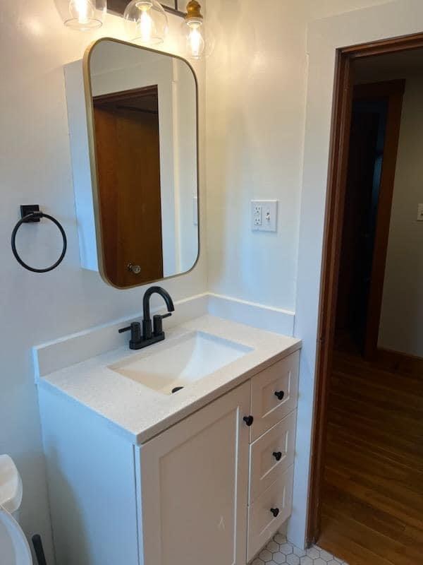 Bathroom vanity with matte-black fixtures, a gold-framed mirror and hex floor tile, Woburn