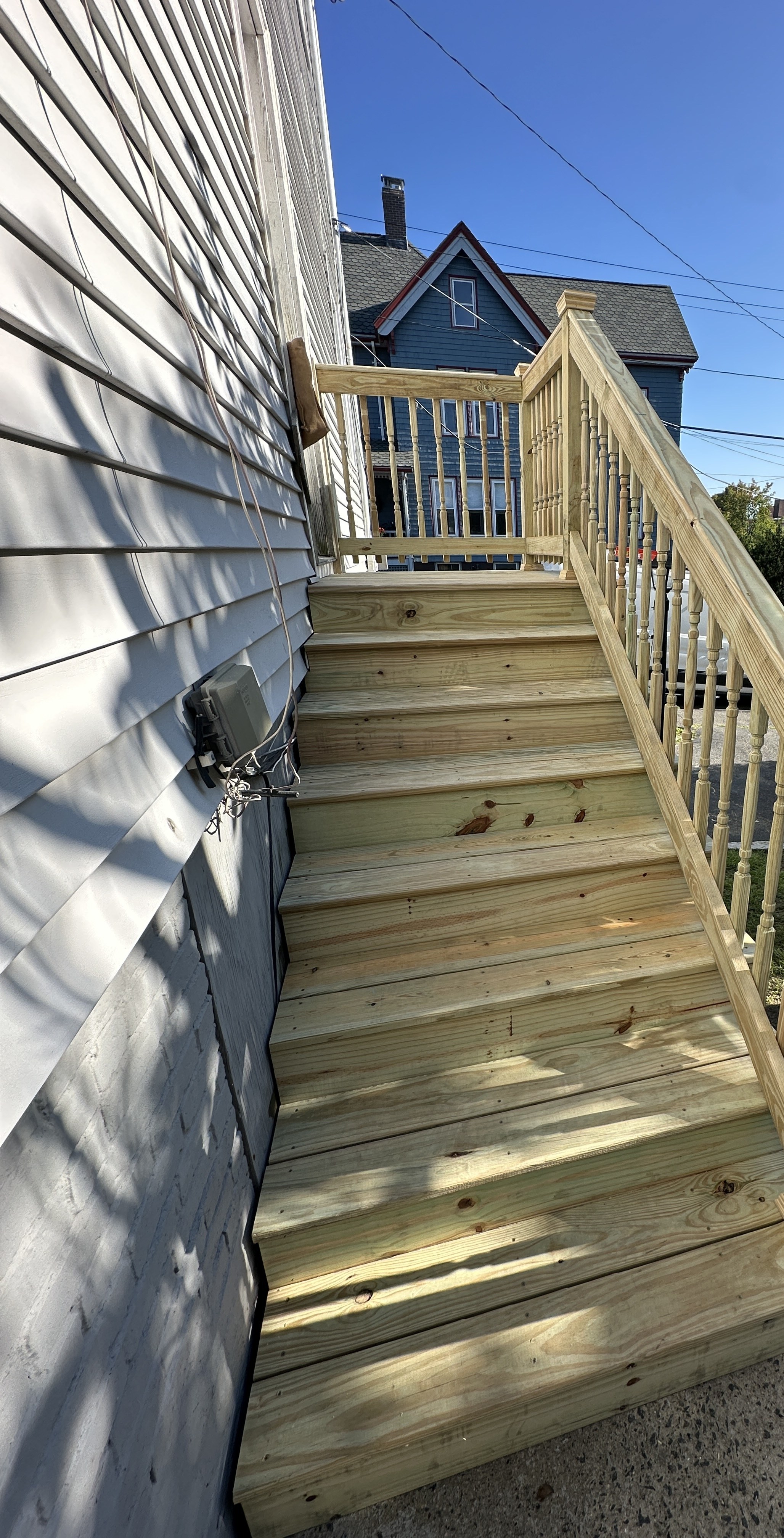 Newly rebuilt exterior staircase with pressure-treated railings and balusters, a neighboring house visible beyond