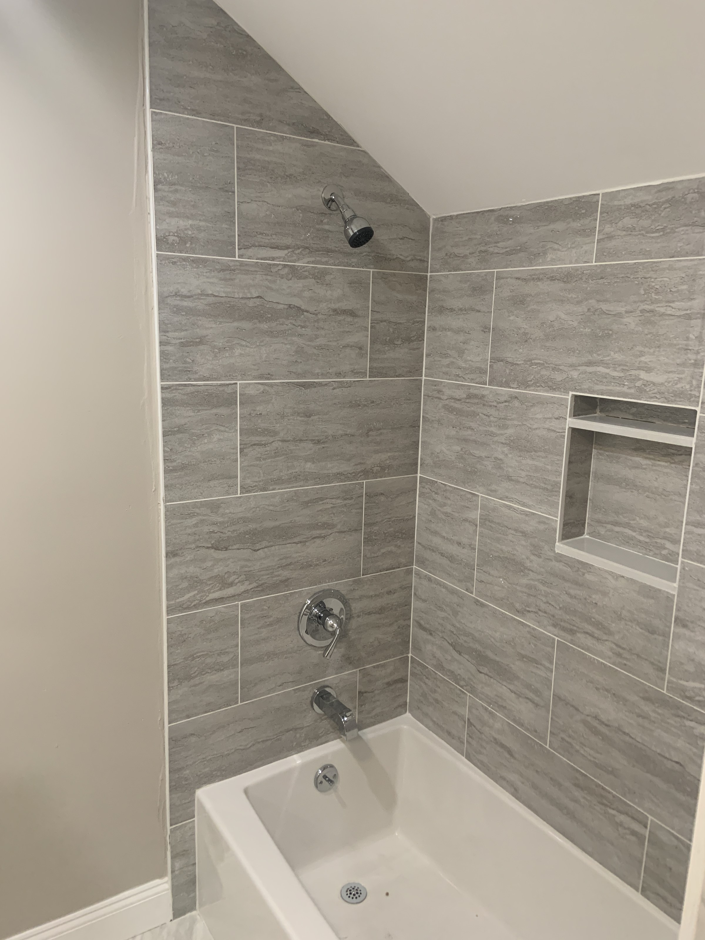 Tub and shower with gray marble-look tile, chrome fixtures and a tiled niche shelf