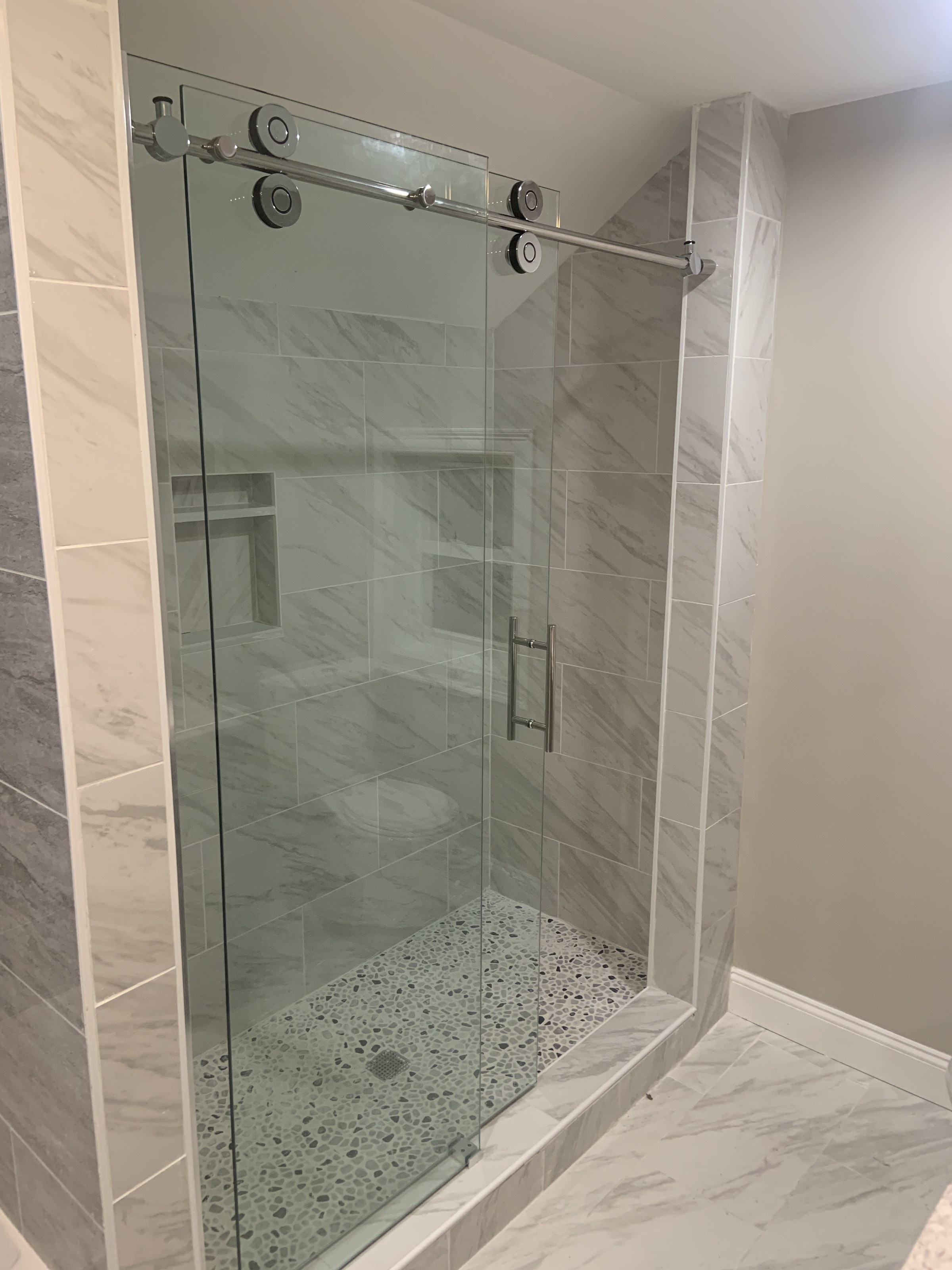 Bathroom with a frameless sliding glass shower door, pebble-tile floor and marble tile