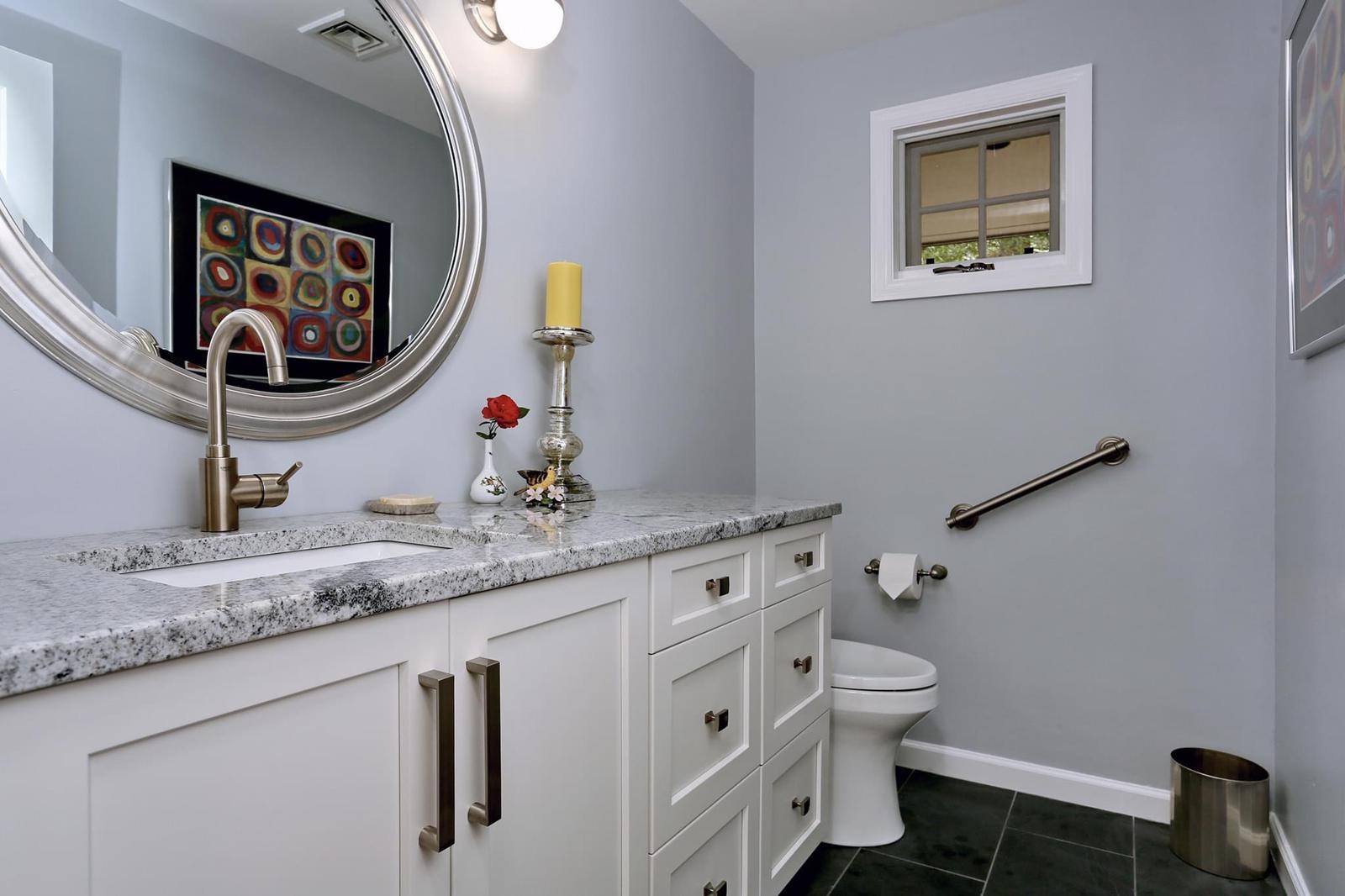 Bathroom with granite counter, white shaker vanity and a round mirror