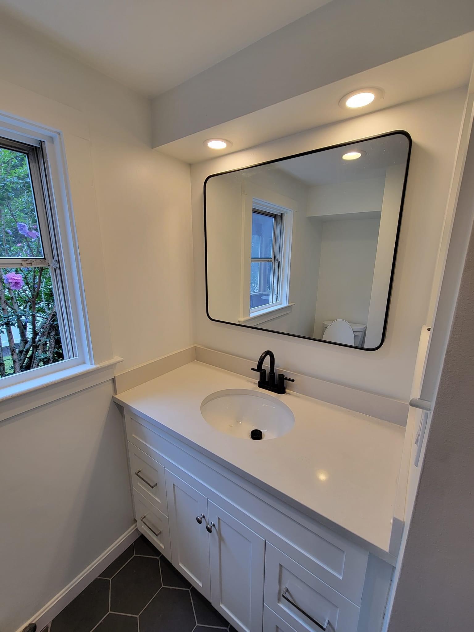 A bathroom with dark hex floor, white vanity and black round mirror and fixtures, Reading