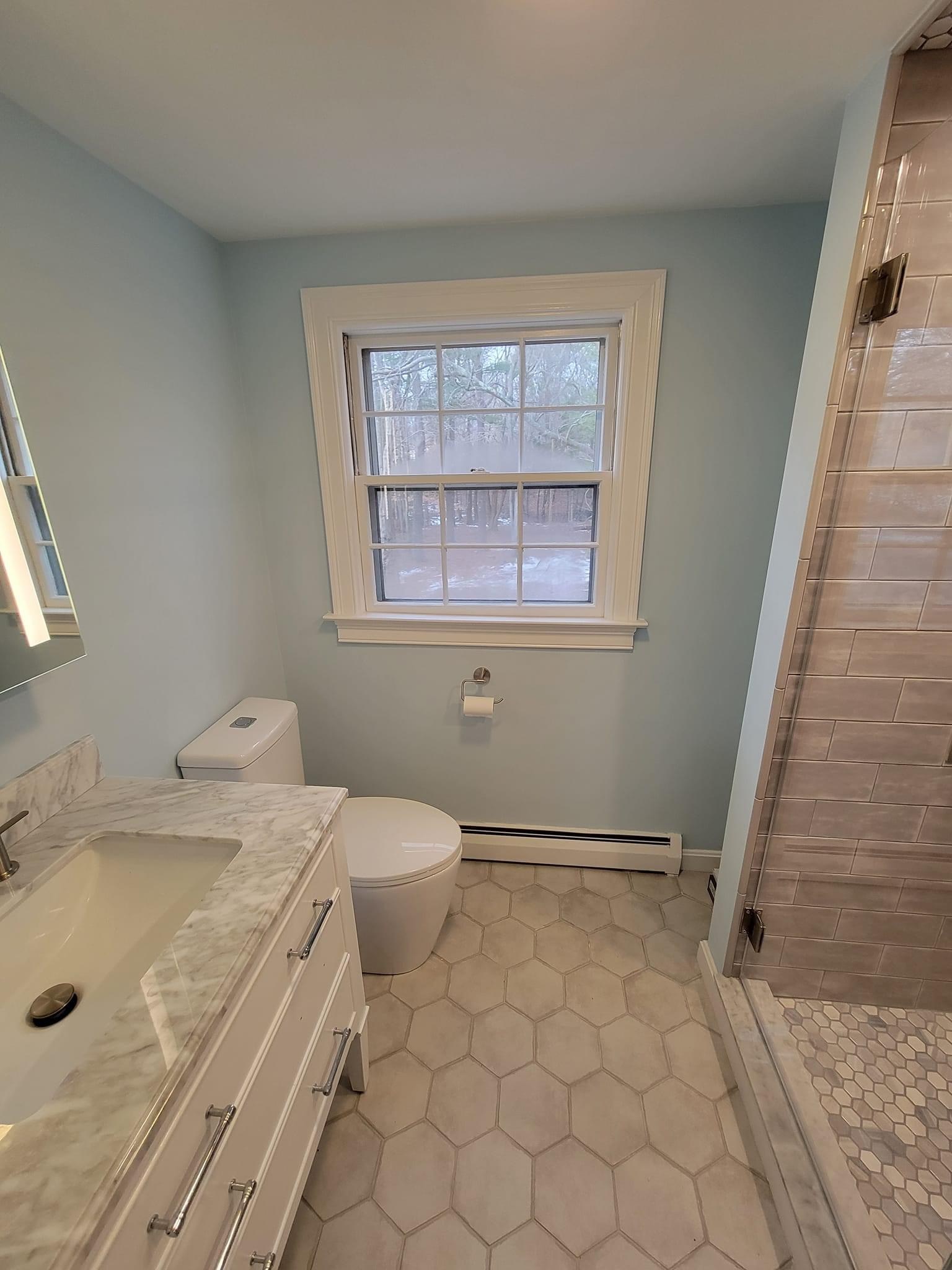 Bathroom with light blue walls, hex floor, marble vanity and tan subway shower tile, Woburn
