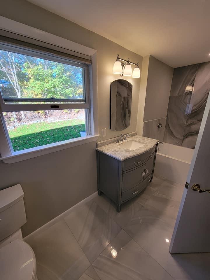 Bathroom with a curved gray vanity and dramatic marble-look shower/tub surround, North Reading