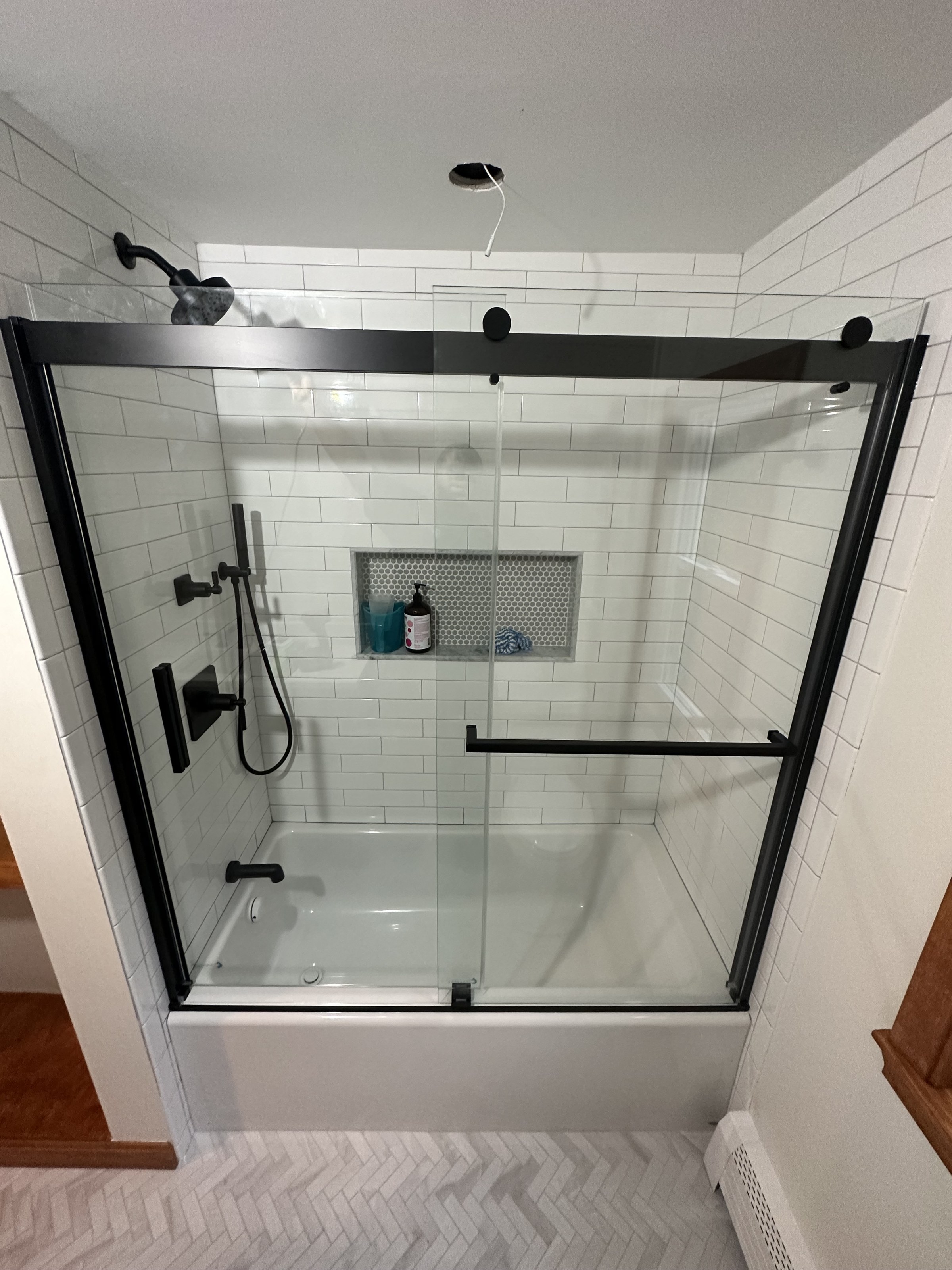 Companion angle of the black-framed glass shower, herringbone floor tile, Woburn