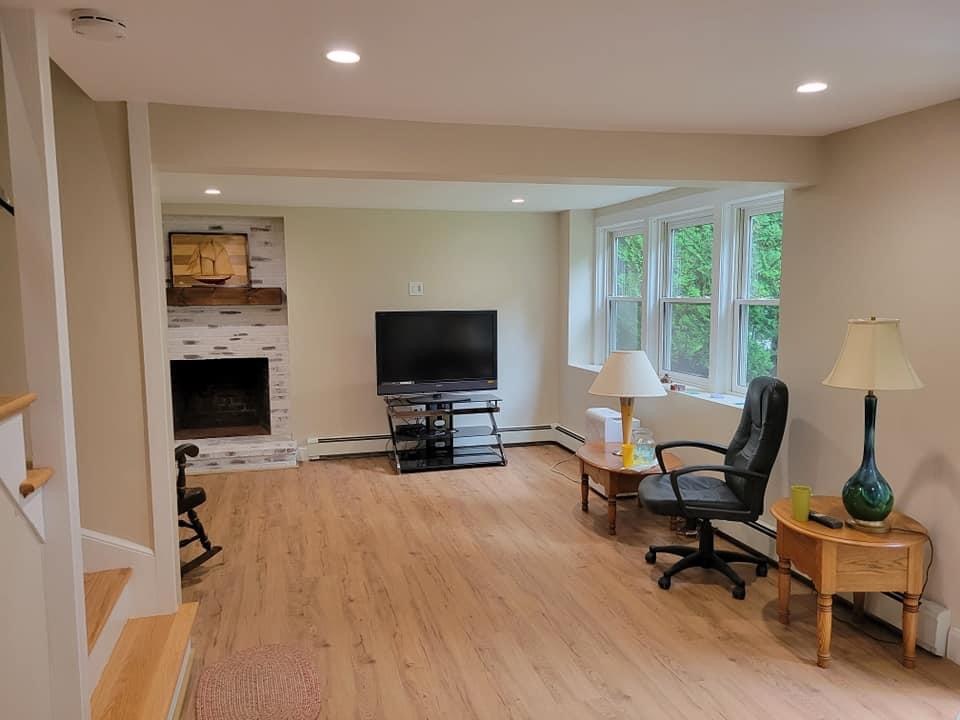 Finished basement family room with a whitewashed brick fireplace, staircase and new flooring, Lynnfield